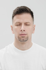 The face of a bearded brunet man in white clothes, eyes closed close up.