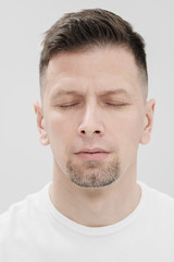 Obraz premium The face of a bearded brunet man in white clothes, eyes closed close up.