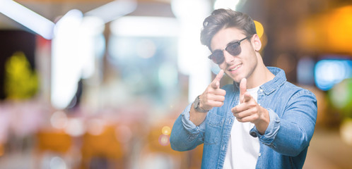 Young handsome man wearing sunglasses over isolated background pointing fingers to camera with happy and funny face. Good energy and vibes.