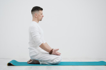 Male brunette with a beard in white clothes on a white background with his hands folded on his chest. Meditation and prayer, yoga.