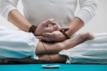 The concept of yoga and meditation. Close-up of the hands and feet of a man in white clothes on a...