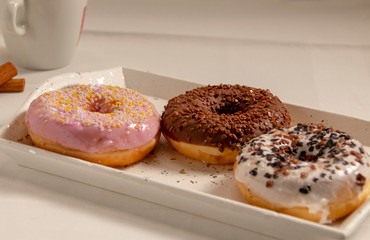three donuts on a white tray with a cup of coffee