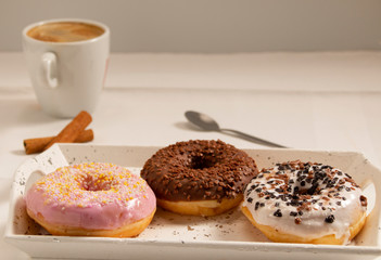 three donuts on a white tray with a cup of coffee