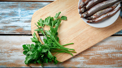 capelin dish on a cutting board with parsley, garlic on a white and blue wooden background