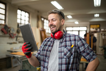 Professional woodworker using tablet in carpentry workshop.