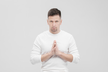 A man in white clothes on a white background with his hands folded on his chest. Meditation and prayer, yoga.