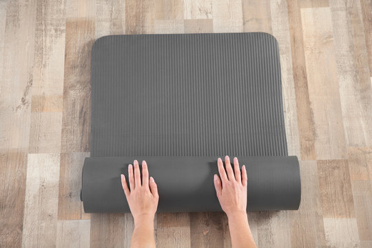 Woman rolling yoga mat on floor indoors, top view