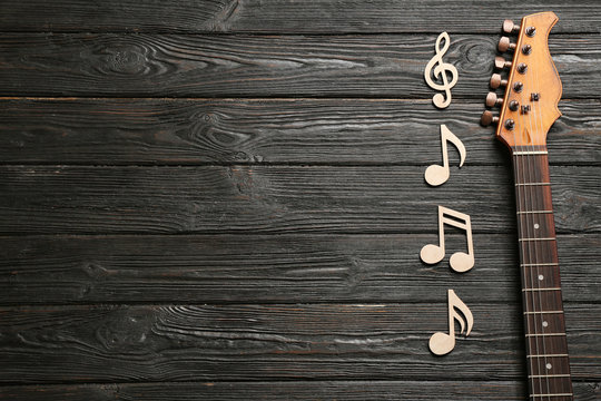 Music notes and guitar neck on wooden background, top view. Space for text