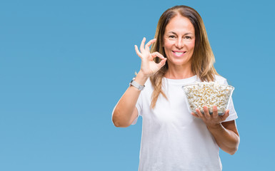 Middle age hispanic woman eating popcorn over isolated background doing ok sign with fingers, excellent symbol