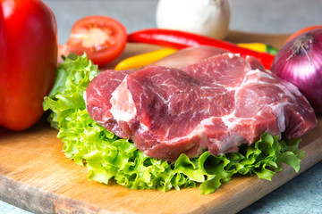 Pork-neck meat steaks on lettuce on background of radishes, tomato, red chili peppers, yellow chili peppers, green paprika, yellow paprika, red paprika, black pepper. Horizontal. Red onions, shallots