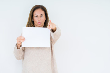 Fototapeta premium Middle age woman holding blank paper sheet over isolated background pointing with finger to the camera and to you, hand sign, positive and confident gesture from the front