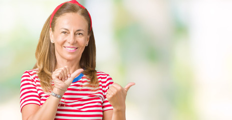 Beautiful middle age woman wearing casual stripes t-shirt over isolated background Pointing to the back behind with hand and thumbs up, smiling confident