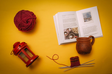 Hygge flat lay with cup, book, knitting needles and tangle, candlestick. Flat lay on yellow background