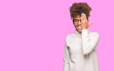 Fototapeta na wymiar Beautiful young african american woman wearing glasses over isolated background covering one eye with hand with confident smile on face and surprise emotion.