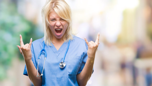 Young beautiful blonde doctor woman wearing medical uniform over isolated background shouting with crazy expression doing rock symbol with hands up. Music star. Heavy concept.