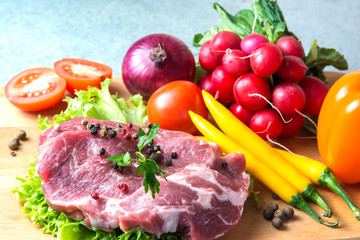Pork-neck meat steaks on lettuce on background of radishes, tomato, red chili peppers, yellow chili peppers, green paprika, yellow paprika, red paprika, black pepper. Horizontal. Red onions, shallots