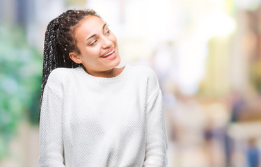 Young braided hair african american girl wearing winter sweater over isolated background looking away to side with smile on face, natural expression. Laughing confident.