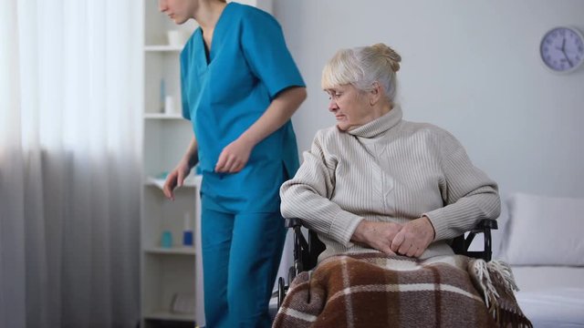 Rude hospital janitor cleaning room, moving wheelchair with old female patient