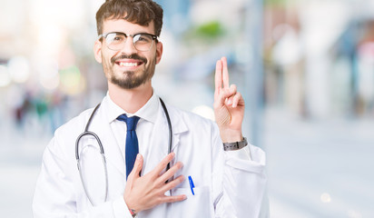 Young doctor man wearing hospital coat over isolated background Swearing with hand on chest and...