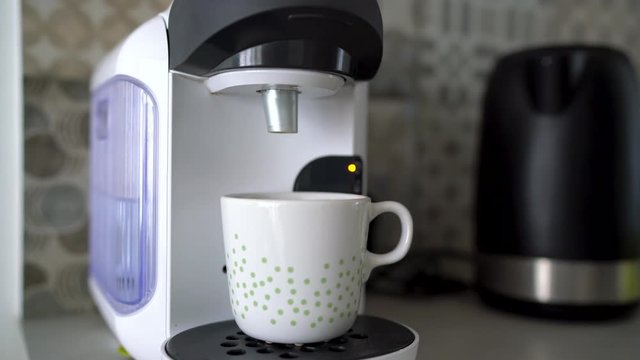 Woman preparing fresh coffee with milk in home capsule coffee machine