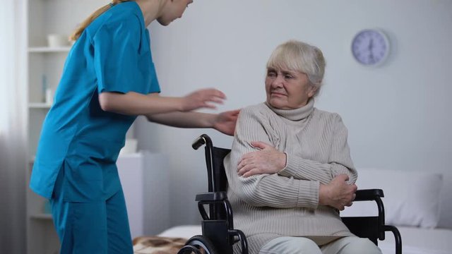 Kind nurse covering with blanket handicapped old woman shivering from cold