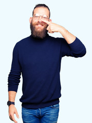 Young blond man wearing glasses and turtleneck sweater Pointing with hand finger to face and nose, smiling cheerful