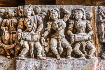 Halebidu, Karnataka, India - November 2, 2013: Hoysaleswara Temple of Shiva. Closeup of music band with dancing girls sculpture as a ribbon along wall of sanctuary. Gray brownish stone..