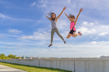 Fototapeta na wymiar Mother and daughter challenge to see who can jump the highest from the seawall on a bright sunny day. Living the active healthy life style is fun for the whole family.