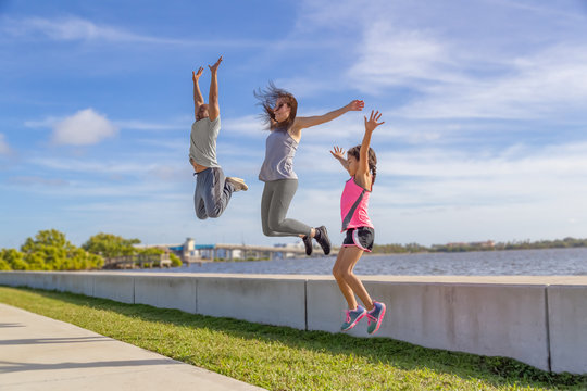 A Family Of Three Challenge To See Who Can Jump The Highest From The Seawall On A Bright Sunny Day. Part Of A Healthy Life Style Is A Good Way To Pass On Family Values To Your Kids.