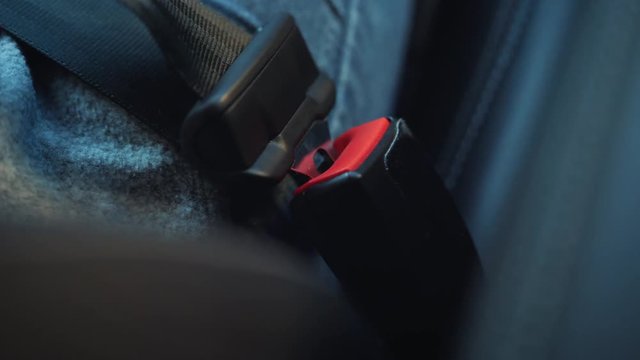 Female hand fastening car safety seat belt while sitting inside of vehicle before driving