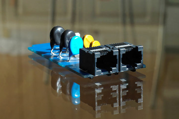 Piece of electronic equipment - black, blue and yellow electronic components mounted on PCB - printed circuit board with network or phone sockets in front side.