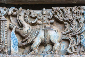 Halebidu, Karnataka, India - November 2, 2013: Hoysaleswara Temple of Shiva. Closeup of elephant and man on top statues on side of the temple structure in bluish stone and some brown background.