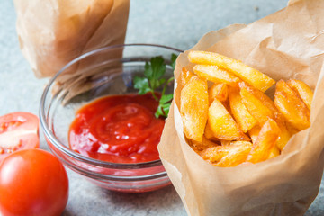 French fries, fried potatoes with ketchup and tomatoes on the background of gray-blue granite.