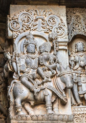 Fototapeta na wymiar Halebidu, Karnataka, India - November 2, 2013: Hoysaleswara Temple of Shiva. Statue on side of main sanctuary, where Lord Shiva and Devi Parvati sit Nandi Bull. Other figures around. Gray stone with b