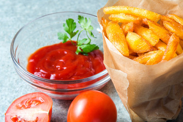 French fries, fried potatoes with ketchup and tomatoes on the background of gray-blue granite.