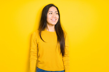 Beautiful brunette woman over yellow isolated background looking away to side with smile on face, natural expression. Laughing confident.