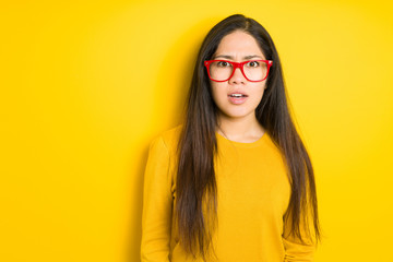Beautiful brunette woman wearing red glasses over yellow isolated background afraid and shocked with surprise expression, fear and excited face.