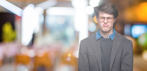 Young handsome business man wearing glasses over isolated background skeptic and nervous, disapproving expression on face with crossed arms. Negative person.