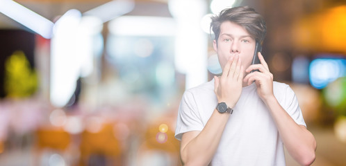 Young man talking on smartphone over isolated background cover mouth with hand shocked with shame for mistake, expression of fear, scared in silence, secret concept