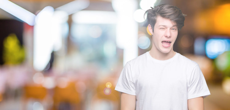 Young handsome man wearing casual white t-shirt over isolated background winking looking at the camera with sexy expression, cheerful and happy face.