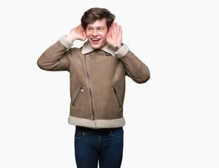 Young handsome man wearing winter coat over isolated background Trying to hear both hands on ear gesture, curious for gossip. Hearing problem, deaf