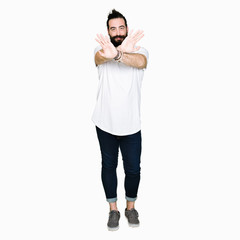 Young hipster man with long hair and beard wearing casual white t-shirt Rejection expression crossing arms and palms doing negative sign, angry face