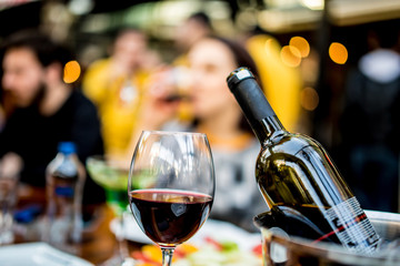 red wine glass and bottle  with ice bucket infront of blurred wine drinking girl