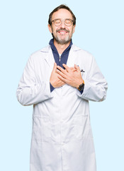 Middle age therapist wearing white coat smiling with hands on chest with closed eyes and grateful gesture on face. Health concept.