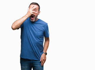 Fototapeta premium Middle age hoary senior man over isolated background peeking in shock covering face and eyes with hand, looking through fingers with embarrassed expression.