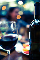 wine bottle with wine glass of red wine front of blurred young couple