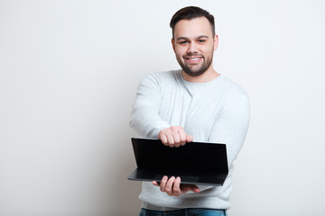 Portrait of young happy man opening laptop over white background.