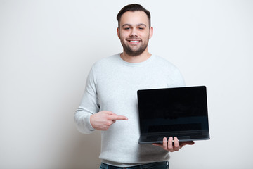 Portrait of young smiling man pointing on laptop over white background.