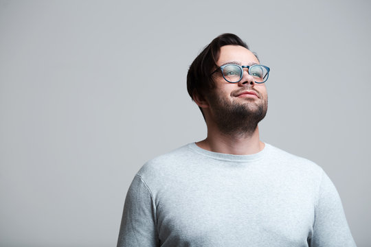 Portrait Of Young Man Wearing Blue Glasses, Looking Up Over White Background.