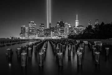Pier pilings and the Tribute in Light over the Manhattan skyline at night, seen from Brooklyn...